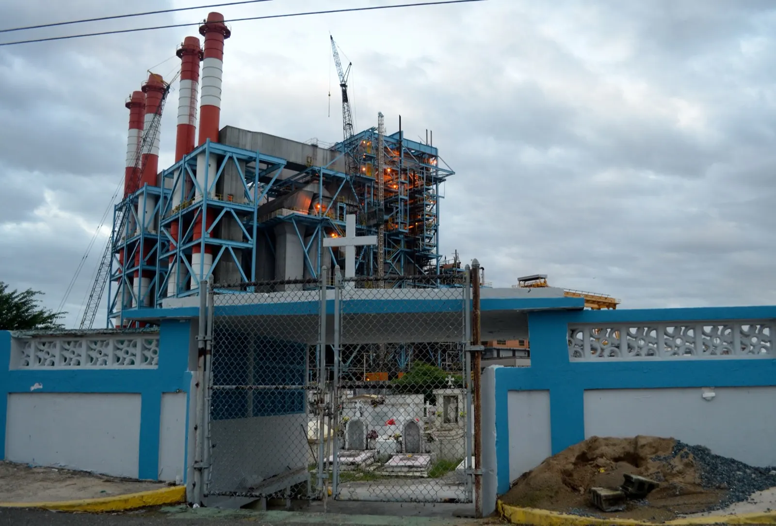 The Palo Seco power plant's red and white stacks rise behind a blue cemetery wall across the bay from San Juan.